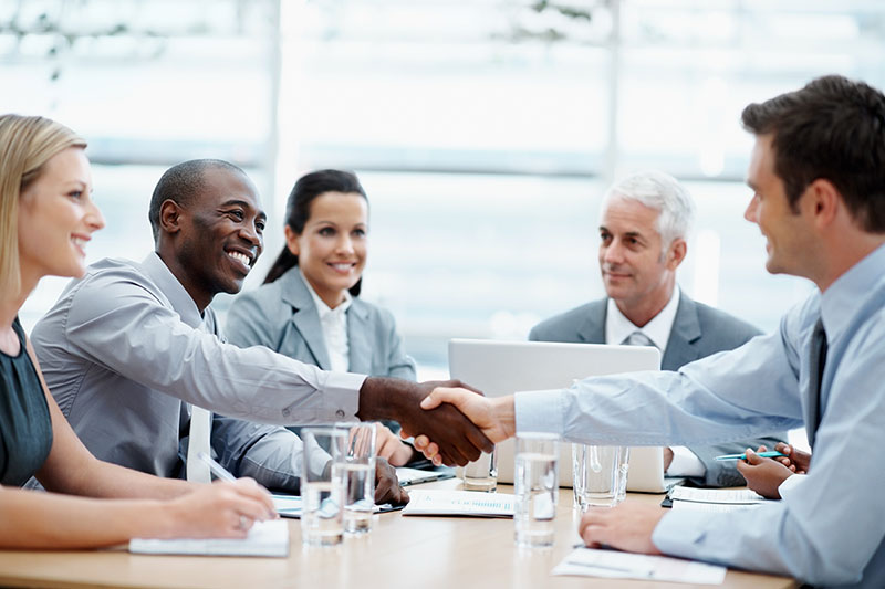 business men and women around a table shaking hands